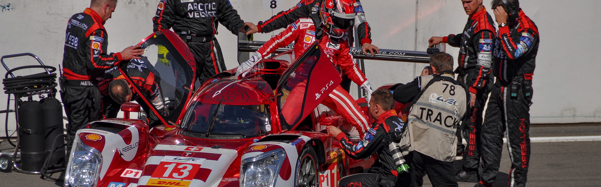 Race driver, engineer, and pit crew communicating with RayTalk racing headsets during a motorsport event